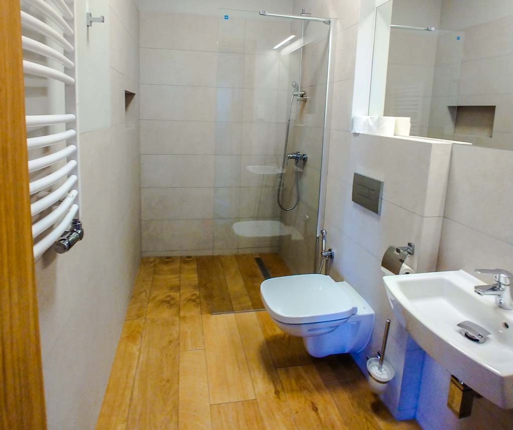 Nowoczesna łazienka po remoncie w Poznaniu, z drewnopodobną podłogą, kabiną prysznicową ze szkła i białymi elementami wyposażenia.