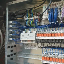 Rozdzielnica elektryczna z widocznymi modułami WAGO, okablowaniem w kolorach niebieskim, czarnym i zielono-żółtym, oraz oznaczeniami na listwach zaciskowych.