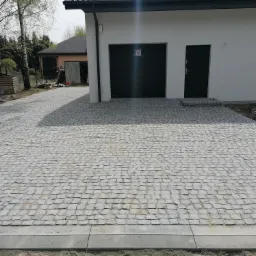 Ułożona kostka granitowa na podjeździe przed domem z garażem, widoczne delikatne krzywizny chodnika i betonowe obrzeża.