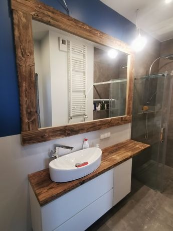 Nowoczesna łazienka z umywalką nablatową, drewnianym blatem i lustrem w rustykalnej ramie z surowego drewna, kabina prysznicowa w tle.
