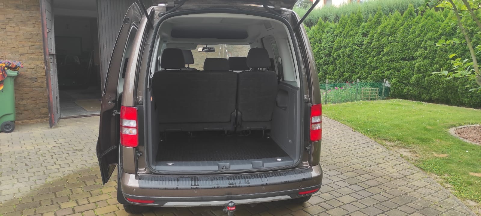 Brązowy van z otwartymi drzwiami bagażnika i bocznymi, widoczne tylne siedzenia i pusta przestrzeń bagażowa, hak holowniczy