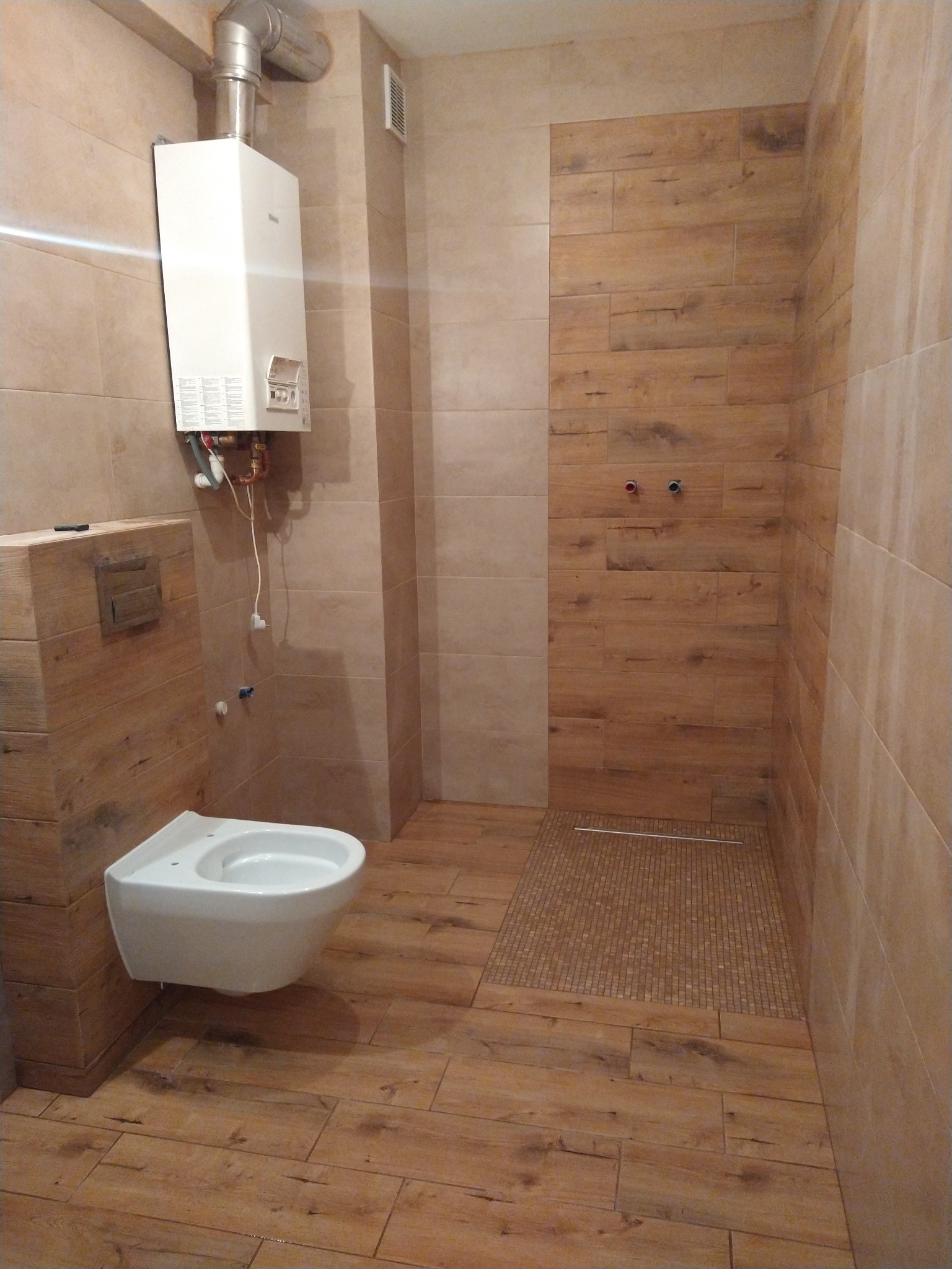 Nowoczesna łazienka z płytkami imitującymi drewno, wiszącą toaletą i grzejnikiem gazowym na ścianie.