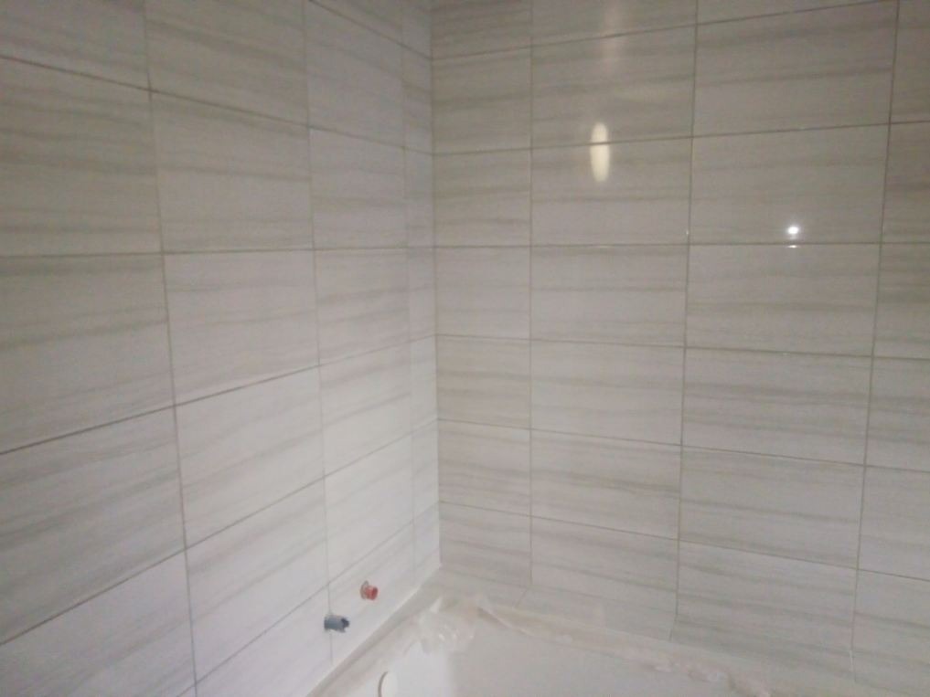 Wnętrze łazienki w trakcie remontu, ściany wyłożone jasnymi, podłużnymi płytkami imitującymi marmur, widoczne wystające rury instalacji wodnej.