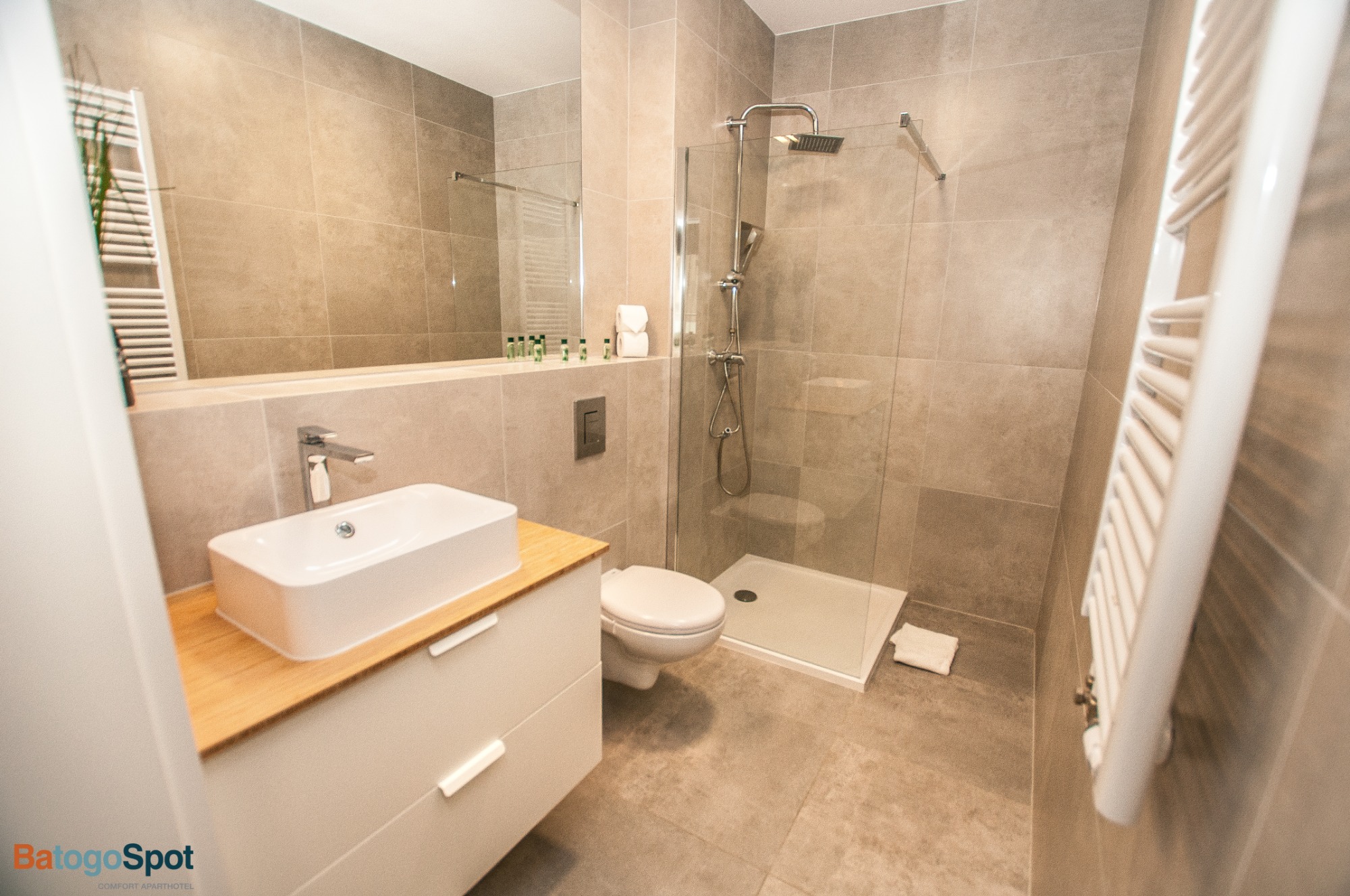 Nowoczesna łazienka w apartamencie z kabiną prysznicową typu walk-in, umywalką nablatową na drewnianym blacie i grzejnikiem drabinkowym.