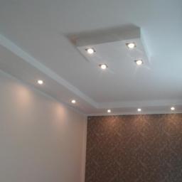 USŁUGI BUDOWLANE A - ZBUD KATARZYNA GRUSZKA - Nowoczesny sufit podwieszany z oświetleniem punktowym LED i dekoracyjną ścianą z brązową tapetą w abstrakcyjny wzór. Na suficie widoczne rury instalacyjne.