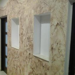 USŁUGI BUDOWLANE A - ZBUD KATARZYNA GRUSZKA - Ściana w korytarzu pokryta dekoracyjnym tynkiem w odcieniach beżu i brązu, z dwoma wnękami pomalowanymi na biało i widocznym fragmentem drzwi po lewej stronie.