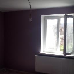 USŁUGI BUDOWLANE A - ZBUD KATARZYNA GRUSZKA - Wnętrze po malowaniu ścian na fioletowo w Świdnicy. Widoczne okno z otwartym skrzydłem, grzejnik i wisząca żarówka. Świeżo pomalowane ściany.