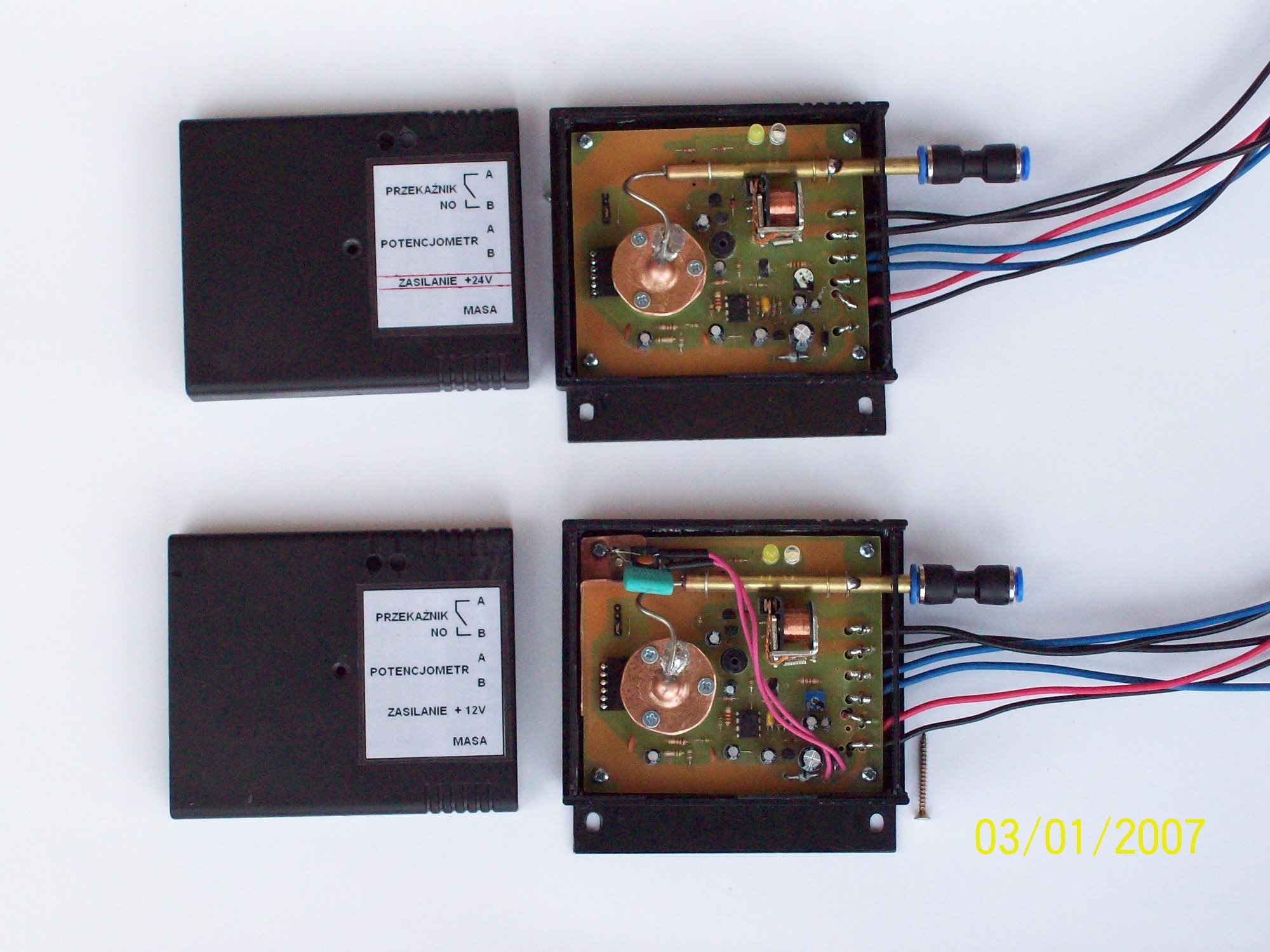 Dwa moduły czujników ciśnienia powietrza z otwartymi obudowami, widoczne płytki drukowane z elementami elektronicznymi, potencjometry oraz przewody zasilające i sygnałowe. Na obudowach naklejki...