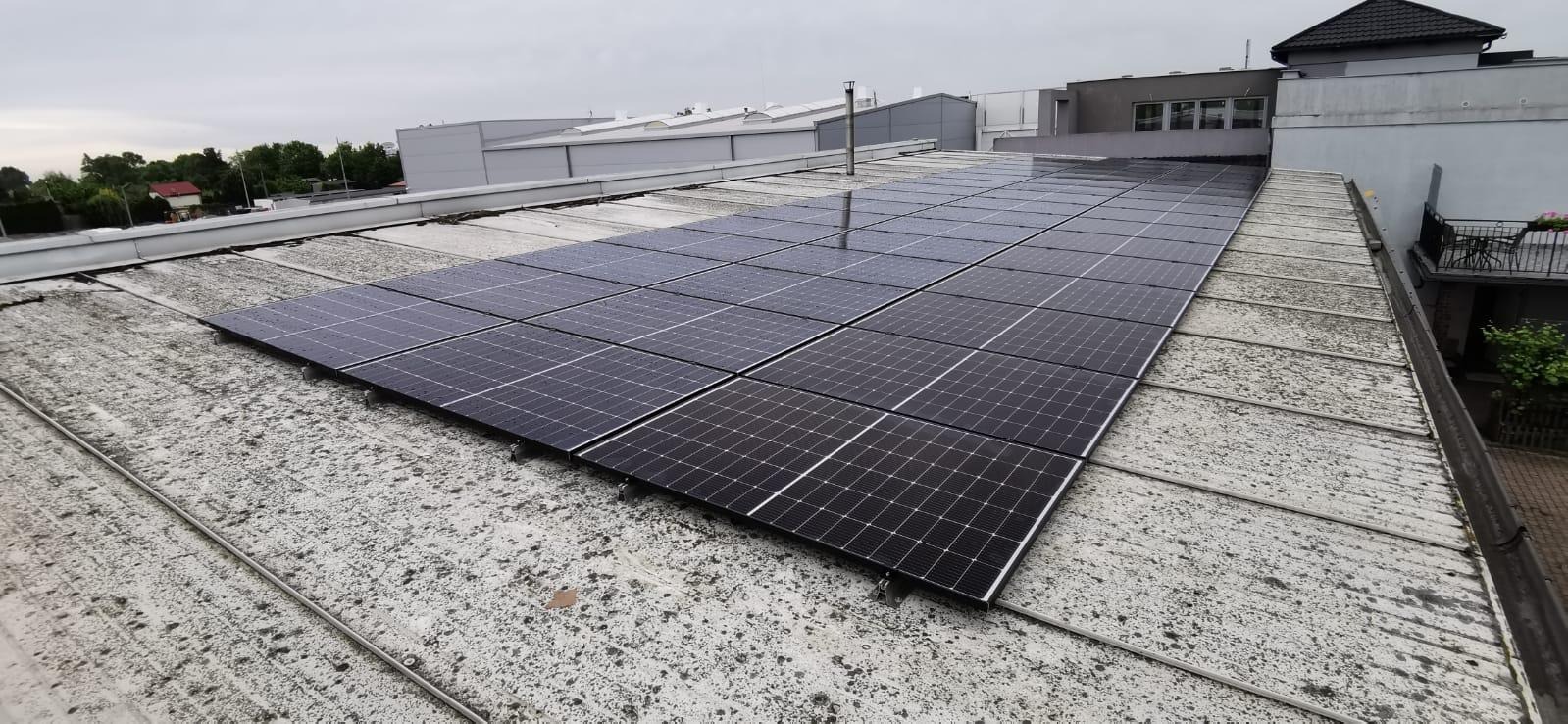 Panel fotowoltaiczny zamontowany na płaskim, zabrudzonym dachu budynku przemysłowego w pochmurny dzień.