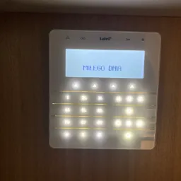 Panel sterowania alarmem firmy Satel z wyświetlanym komunikatem 'Miłego dnia', zamontowany na drewnianej ścianie.