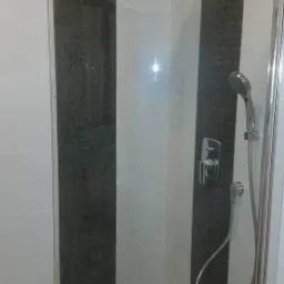 Nowoczesna kabina prysznicowa z deszczownicą i słuchawką, wykończona białymi i grafitowymi płytkami w pionowe pasy.