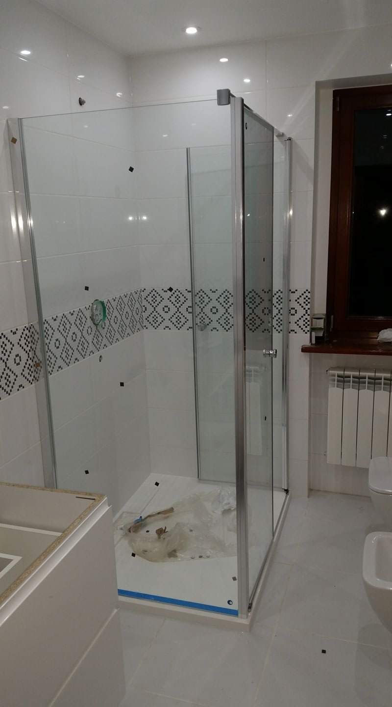 Nowoczesna kabina prysznicowa z przezroczystego szkła i srebrnymi profilami w trakcie montażu w łazience z biało-czarną dekoracją ścienną.