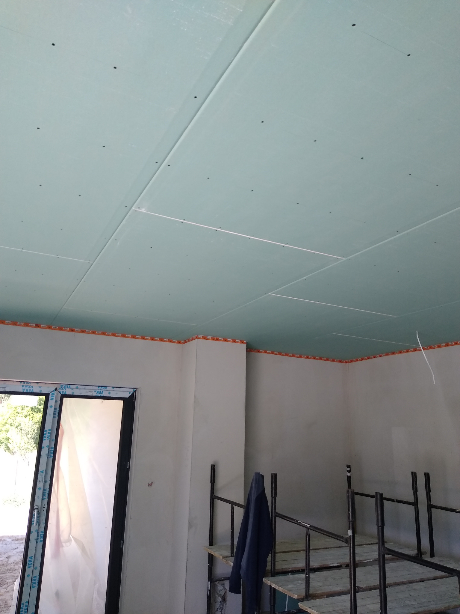 Montaż sufitu podwieszanego z płyty kartonowo-gipsowej w pomieszczeniu w trakcie remontu, widoczne rusztowania i zabezpieczenia narożników.