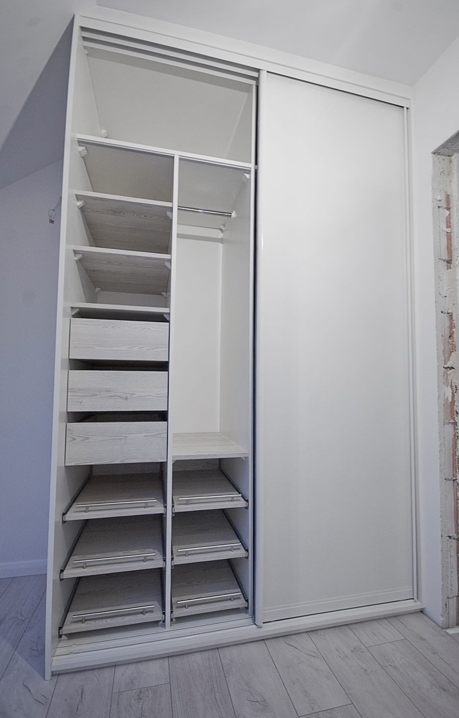 Wnętrze białej szafy przesuwnej z szufladami i półkami z jasnego drewna, widoczne metalowe prowadnice szuflad i drążek na ubrania.