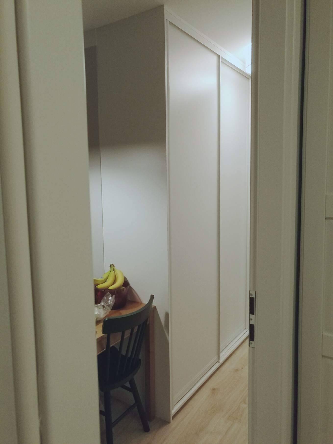 Biała szafa przesuwna wnękowa z widoczną częścią stołu z owocami, widziana zza uchylonych drzwi.