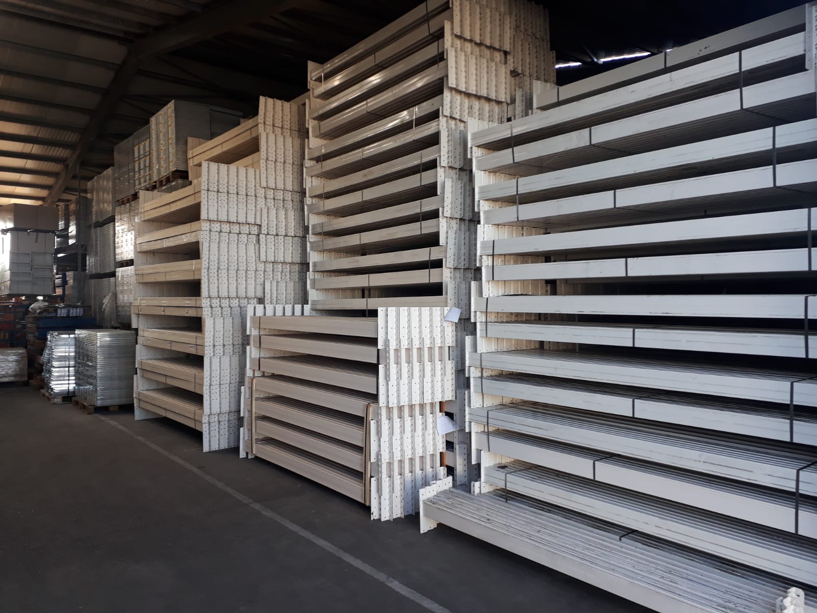 Magazyn pełen palet z metalowymi elementami konstrukcyjnymi, prawdopodobnie przeznaczonymi do montażu regałów magazynowych.