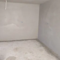 Surowe wnętrze po nałożeniu szarego tynku maszynowego, widoczne gniazdka elektryczne i ślady na podłodze.