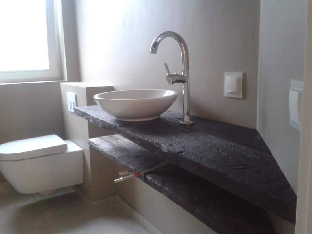 Nowoczesna łazienka z umywalką nablatową na blacie z ciemnego, postarzanego drewna, widoczna toaleta podwieszana i instalacja wodna.