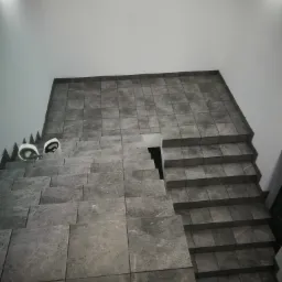 Wykończone płytkami w odcieniach szarości schody wewnętrzne, z dwoma kaskami ochronnymi leżącymi na górnych stopniach, widok z góry.