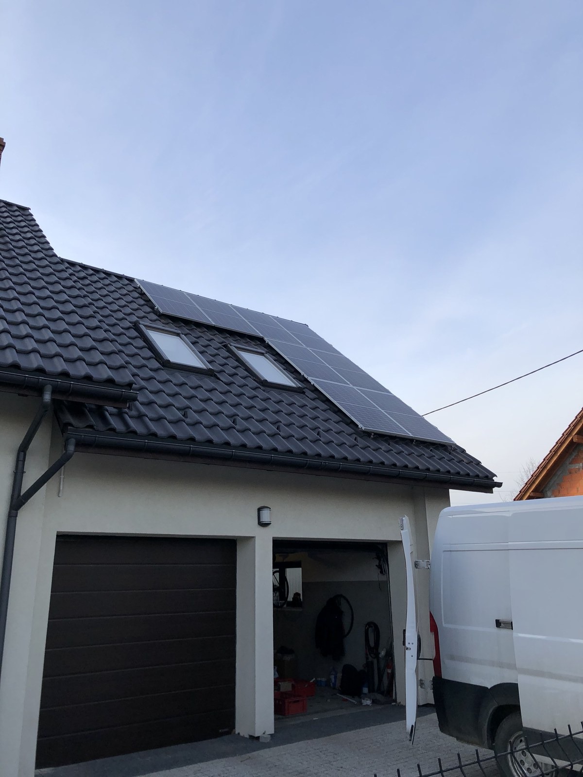 Panele fotowoltaiczne zamontowane na dachu domu w Kobiernicach, widoczne okna dachowe i częściowo otwarty garaż, obok zaparkowany biały bus.