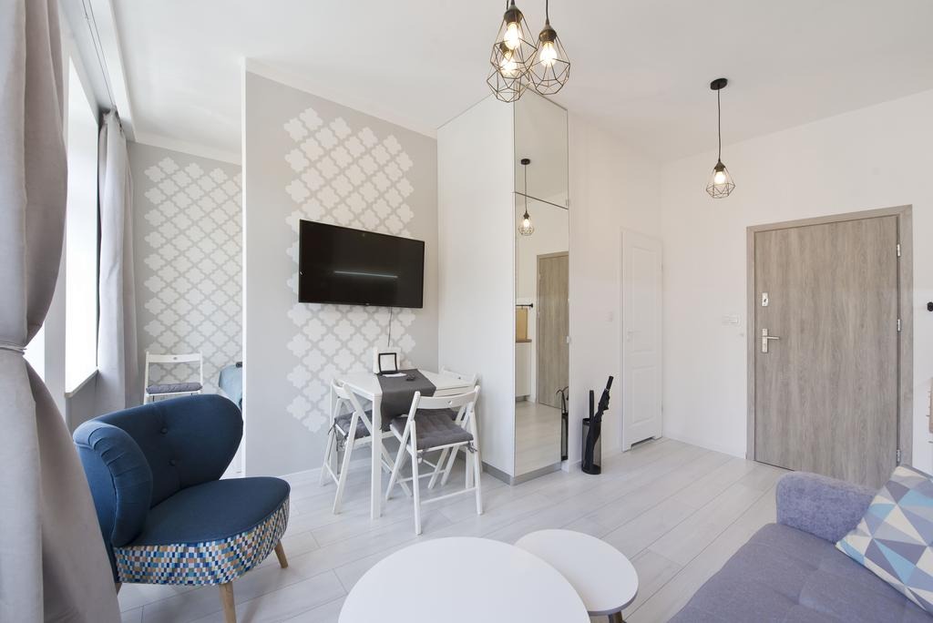 Jasne wnętrze mieszkania w Gdańsku po remoncie: białe ściany z subtelnym wzorem, drewniana podłoga, nowoczesne oświetlenie i minimalistyczne meble.