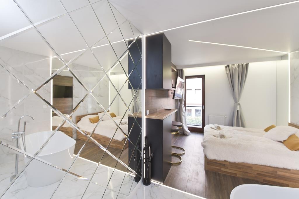Nowoczesne studio: lustrzana ściana z rombów oddziela łazienkę z wanną od części sypialnej z drewnianym łóżkiem i aneksem kuchennym z hokerami.