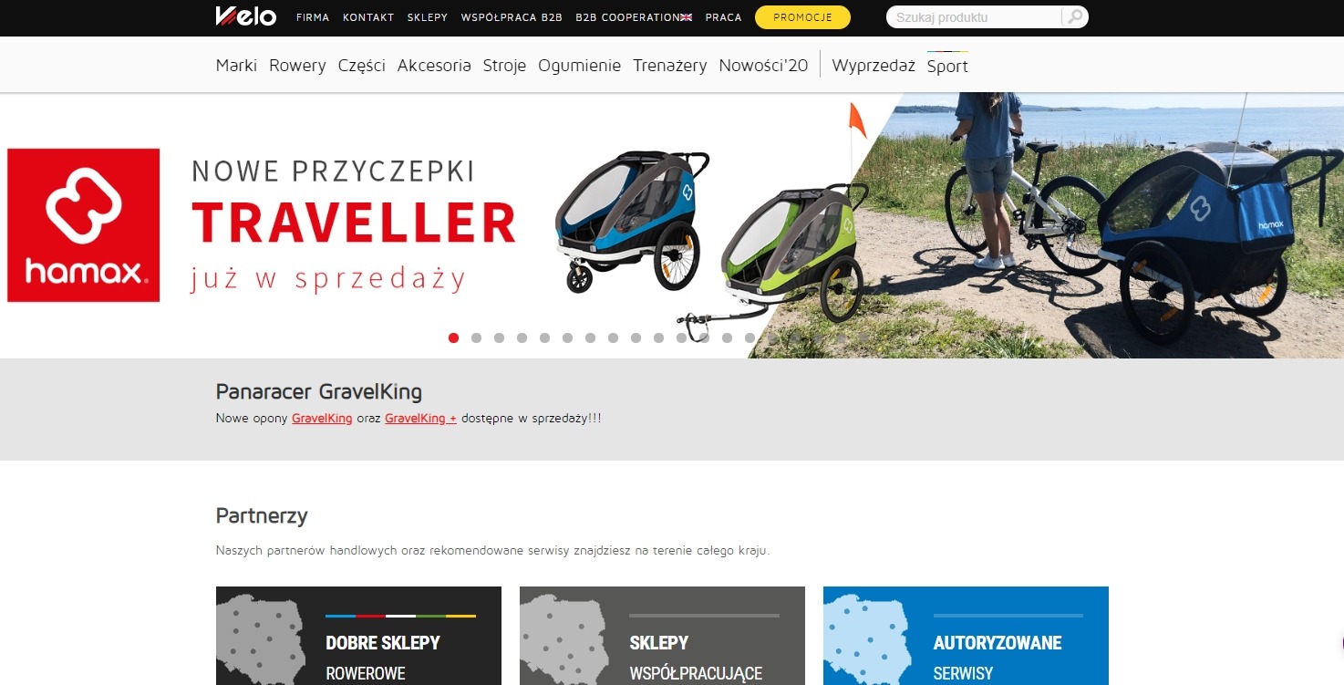 Baner reklamowy sklepu internetowego z przyczepkami rowerowymi Hamax Traveller, prezentujący dwa modele przyczepek w kolorach niebieskim i zielonym, oraz zdjęcie roweru z podpiętą przyczepką na tle...