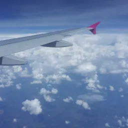 Widok z okna samolotu na skrzydło z różowym zakończeniem, chmury i krajobraz z góry w słoneczny dzień.