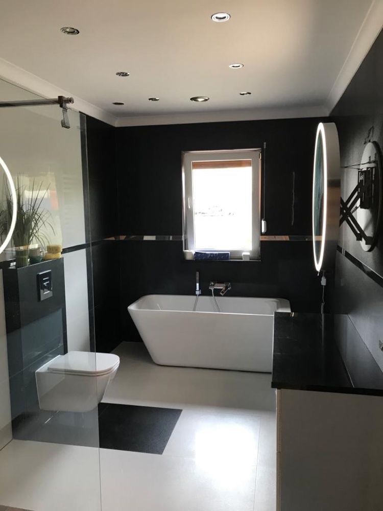 Nowoczesna łazienka z czarno-białymi płytkami podłogowymi, wolnostojącą białą wanną, podwieszaną toaletą, czarnymi ścianami i okrągłymi lustrami z podświetleniem LED.