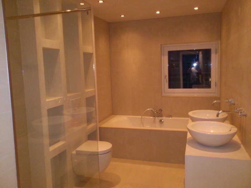 Jasna łazienka z wanną, dwiema okrągłymi umywalkami nablatowymi, toaletą w zabudowie i przeszklonym prysznicem walk-in z wnękami na kosmetyki.