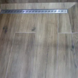 Ułożone płytki imitujące drewno w kabinie prysznicowej z odpływem liniowym i szklaną ścianką prysznicową.