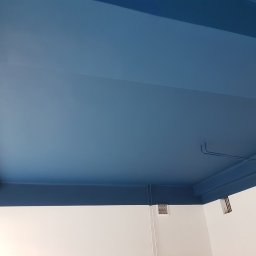 WILLO Marcin Tomaszewski - Pomieszczenie po malowaniu sufitu i górnej części ścian na kolor niebieski, widoczne fragmenty instalacji pod sufitem i kratka wentylacyjna na ścianie.