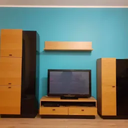 Turkusowa ściana w salonie z meblami w odcieniach drewna i czerni, w tym szafki, półka i szafka RTV z telewizorem.