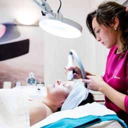 Atelier Fotografii Biznesowej - Zabieg kosmetyczny twarzy wykonywany w Lublińcu w Instytucie Zdrowia i Urody Claria, pacjentka leży na leżance pod lampą, kosmetyczka używa specjalistycznego urządzenia.