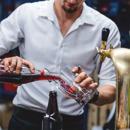 Atelier Fotografii Biznesowej - Barman w białej koszuli nalewa ciemnoczerwony napój z butelki typu swing-top do szklanki, obok widoczny kran do piwa i inne butelki, zdjęcie z eventu dla Wozijadło.pl.