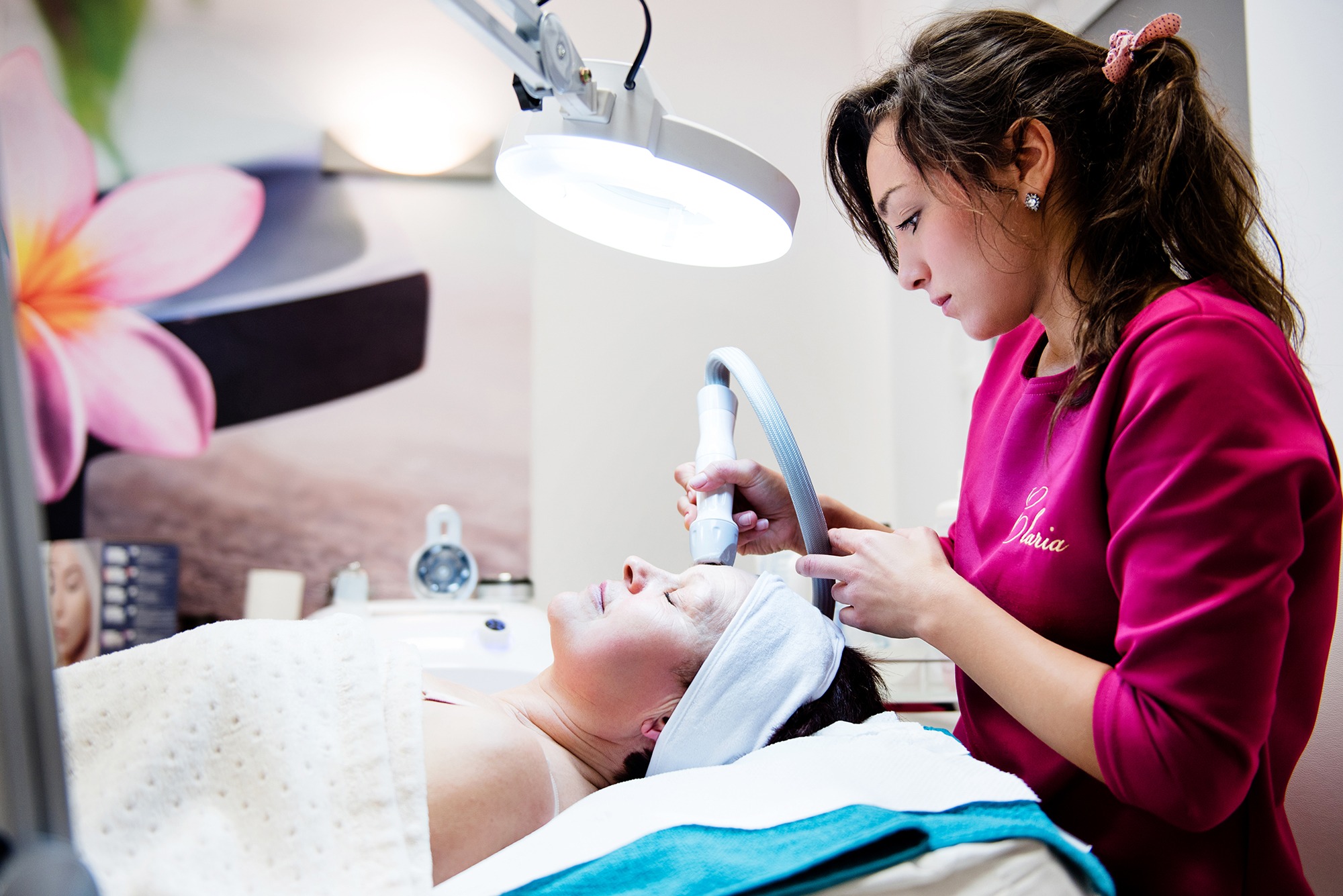 Zabieg kosmetyczny twarzy wykonywany w Lublińcu w Instytucie Zdrowia i Urody Claria, pacjentka leży na leżance pod lampą, kosmetyczka używa specjalistycznego urządzenia.