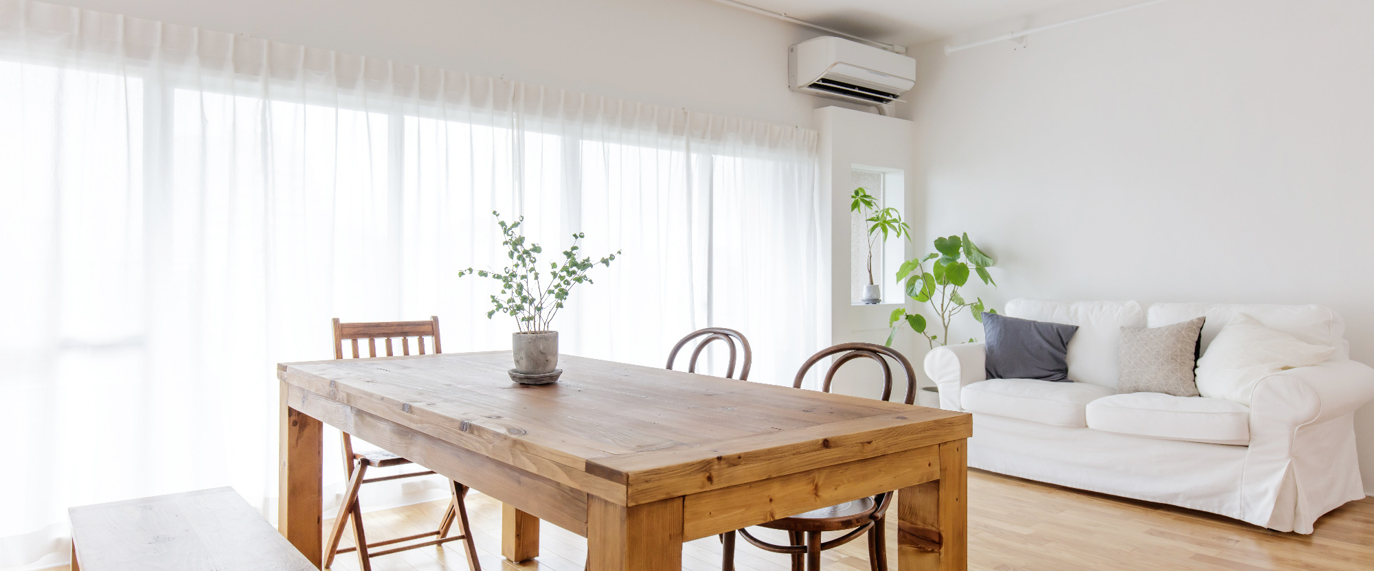 Jasne wnętrze pokoju z drewnianym stołem, krzesłami, białą sofą i klimatyzatorem ściennym