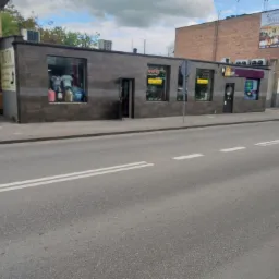 Fasada budynku usługowego z oknami wystawowymi i drzwiami wejściowymi, wykończona płytkami imitującymi kamień, widok z ulicy w dzień.