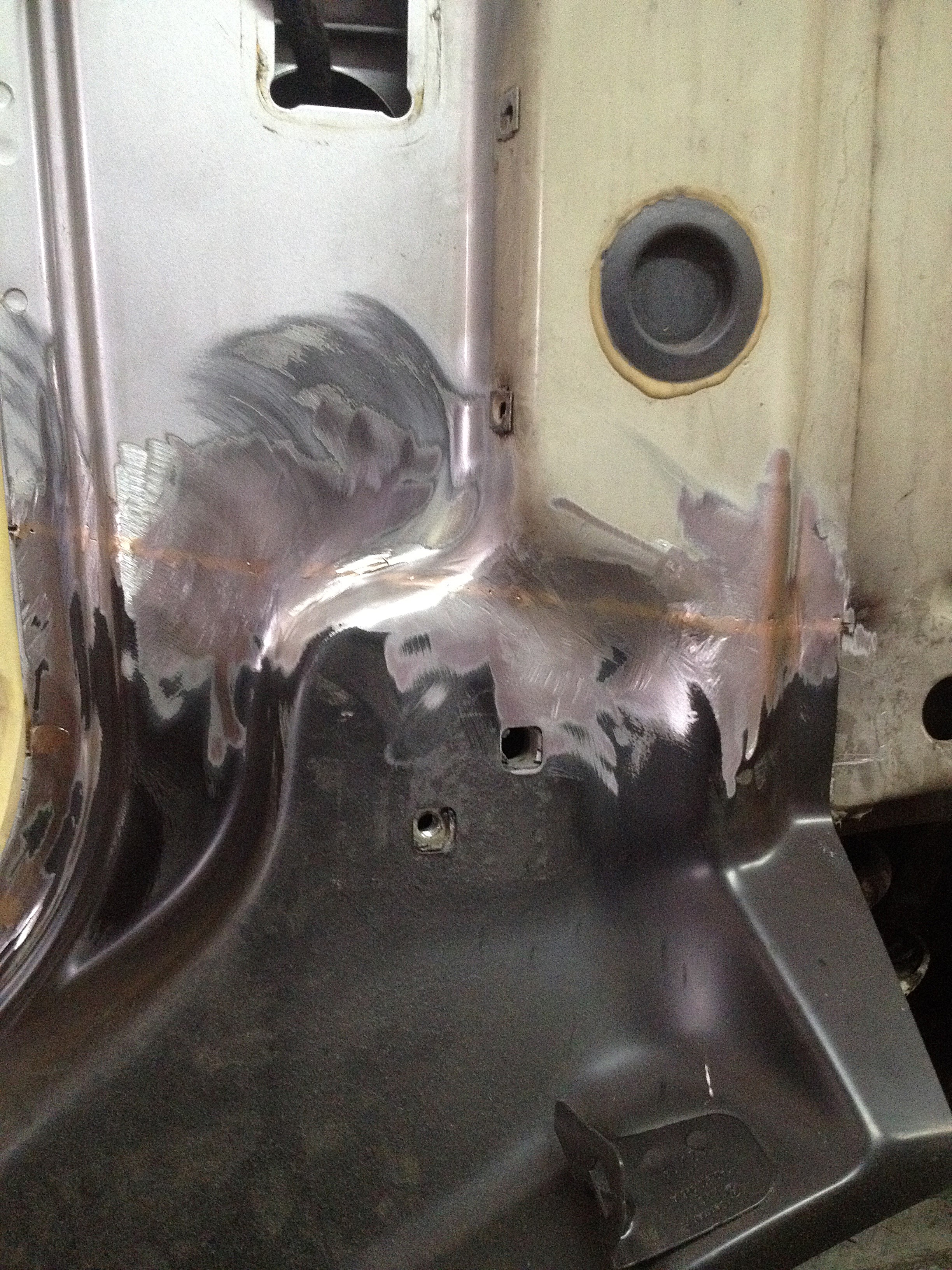 Fragment karoserii samochodu w trakcie naprawy blacharskiej, z widocznymi śladami szlifowania i wypełniania ubytków.