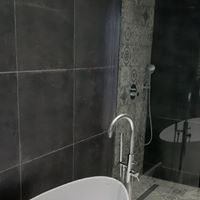 Nowoczesna łazienka z ciemnymi, matowymi płytkami na ścianie i dekoracyjnymi płytkami w strefie prysznica. Bateria umywalkowa chromowana, wysoka, obok wolnostojąca wanna.