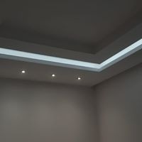 Minimalistyczne oświetlenie sufitowe w narożniku pomieszczenia z trzema punktowymi lampami halogenowymi i ukrytym paskiem LED dającym subtelne, rozproszone światło.