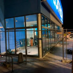 Montaż aluminiowych okien w sklepie Decathlon, widoczne rusztowania i narzędzia wewnątrz budynku, oświetlenie nocne.