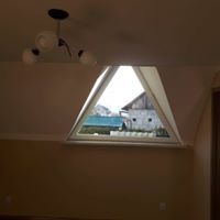 Poddasze z oknem trójkątnym, widok na budynek gospodarczy i góry, sufit ze skosem, lampa sufitowa z trzema kloszami.