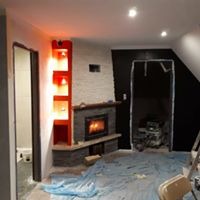 Wnętrze pokoju po remoncie: kominek obłożony kamieniem, czerwona wnęka z półkami, czarna ściana, podłoga zabezpieczona folią malarską, widoczne ślady prac malarskich.