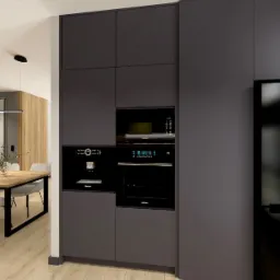 Nowoczesna kuchnia z zabudową w odcieniach szarości, z czarnym sprzętem AGD (lodówka, piekarnik, ekspres do kawy). Drewniany stół z krzesłami w tle.