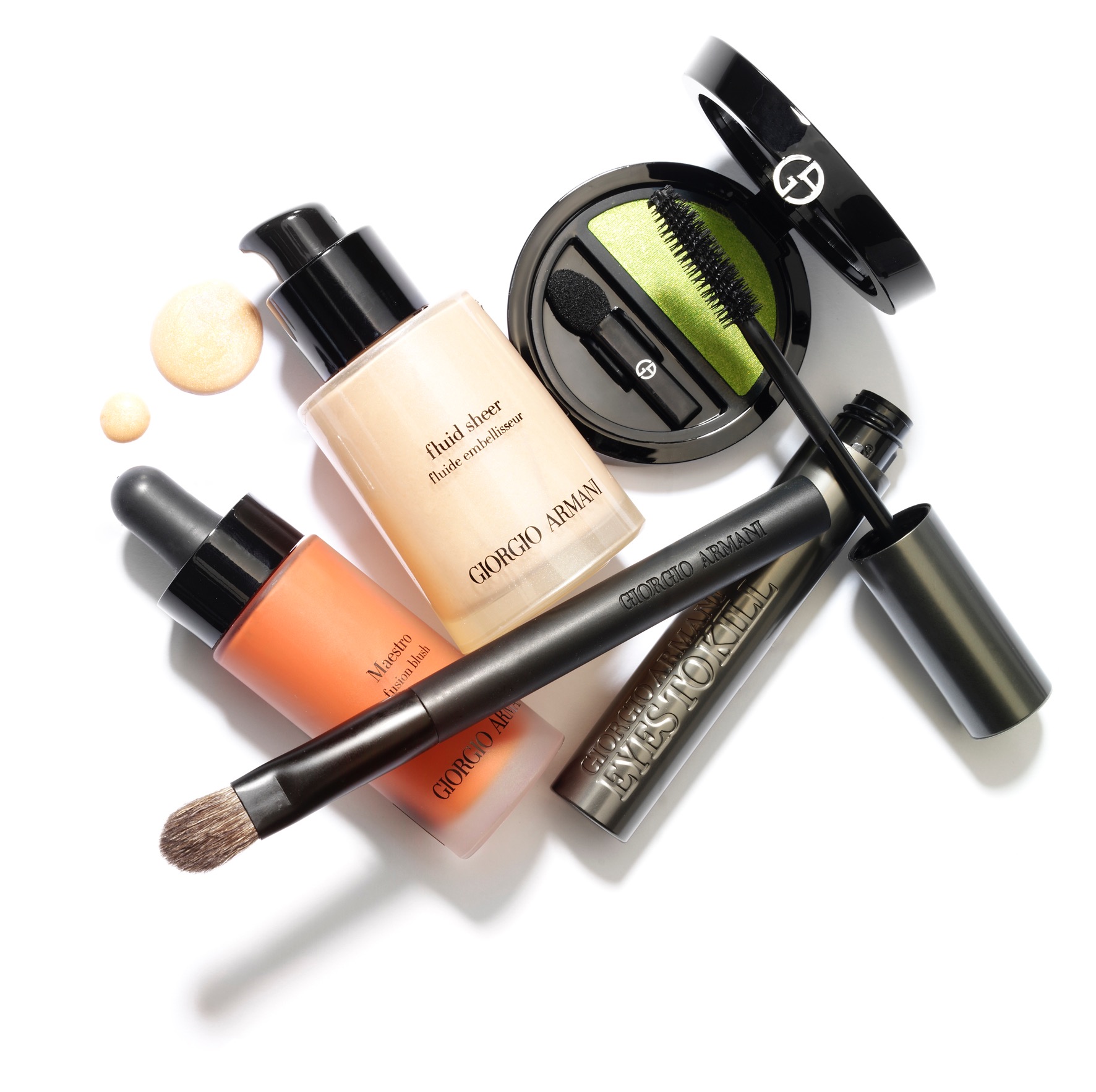 Kompozycja kosmetyków marki Giorgio Armani na białym tle, w tym podkład Fluid Sheer, róż Maestro, tusz do rzęs Eyes to Kill, paleta cieni do powiek i pędzel do makijażu.