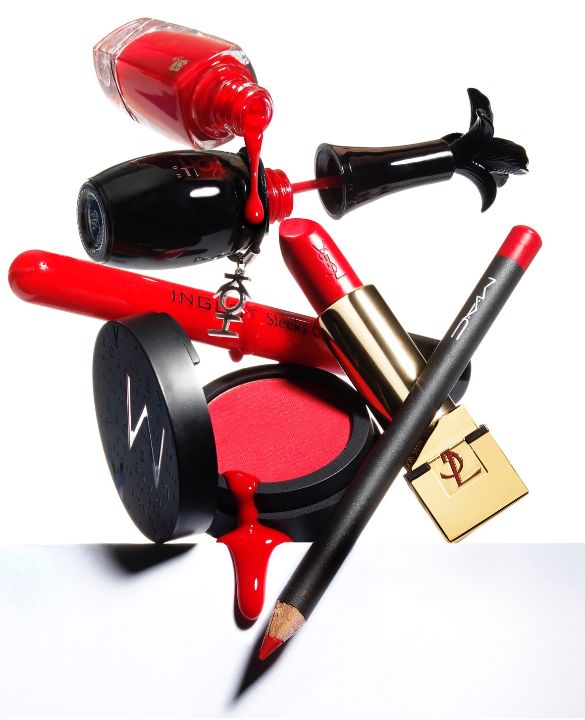 Kompozycja czerwonych kosmetyków: lakier do paznokci wylewający się na puder, szminka, błyszczyk i konturówka, na białym tle, wykonana w Zielonce.