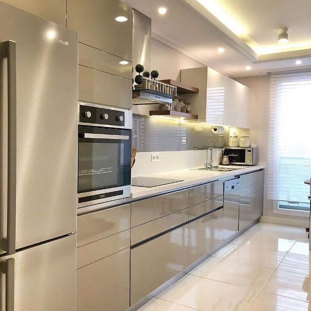 Nowoczesna kuchnia z błyszczącymi, beżowymi frontami szafek, zabudowanym piekarnikiem i lodówką side-by-side, oświetleniem LED pod szafkami wiszącymi i na suficie.