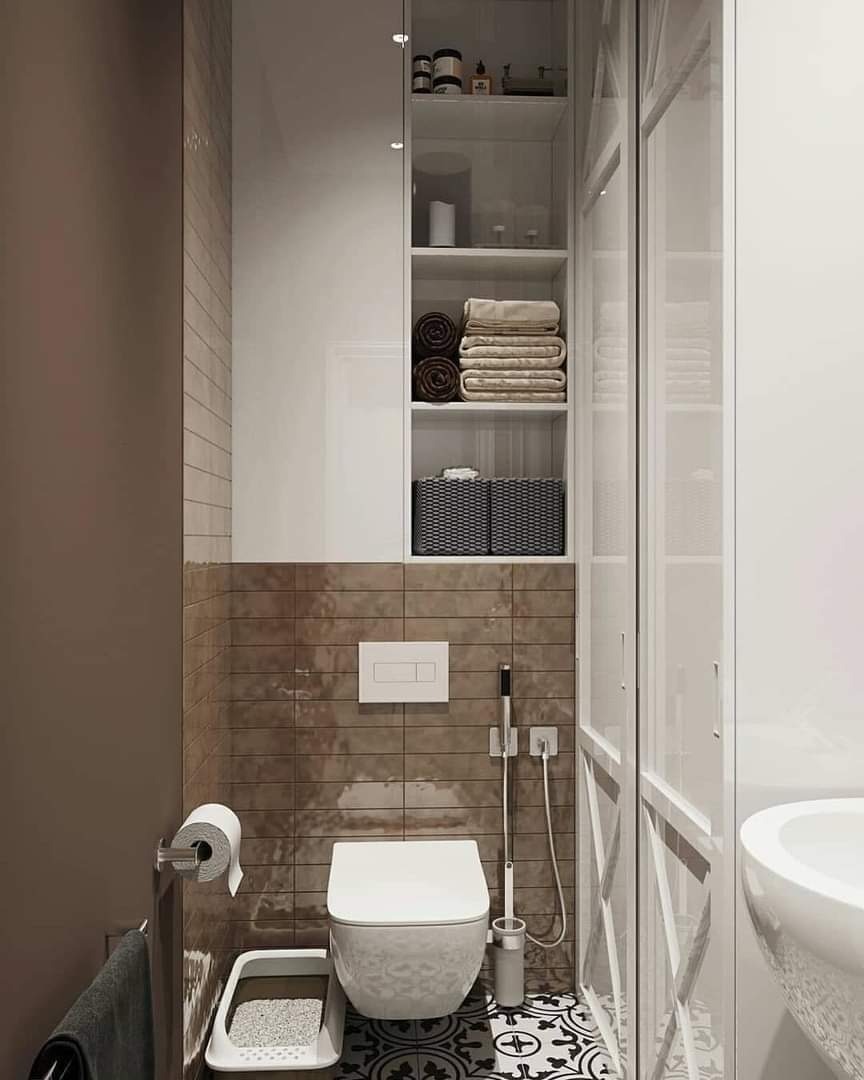Nowoczesna łazienka z brązowymi płytkami imitującymi kamień, białą toaletą, zabudową nad nią z półkami na ręczniki i kosmetyki, oraz czarno-białą podłogą w geometryczne wzory.
