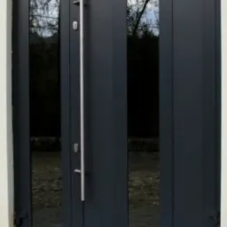 Nowoczesne, grafitowe drzwi wejściowe z trzema przeszkleniami i długim, pionowym uchwytem ze stali nierdzewnej, widok z zewnątrz.